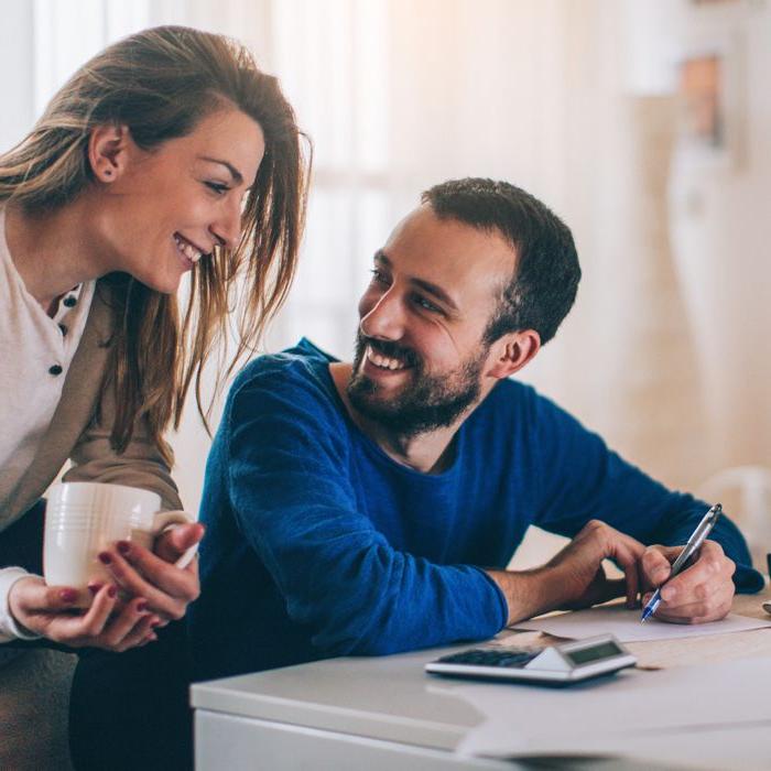 A young couple smiling over the kitchen table using the Patelco Mobile App on their phone